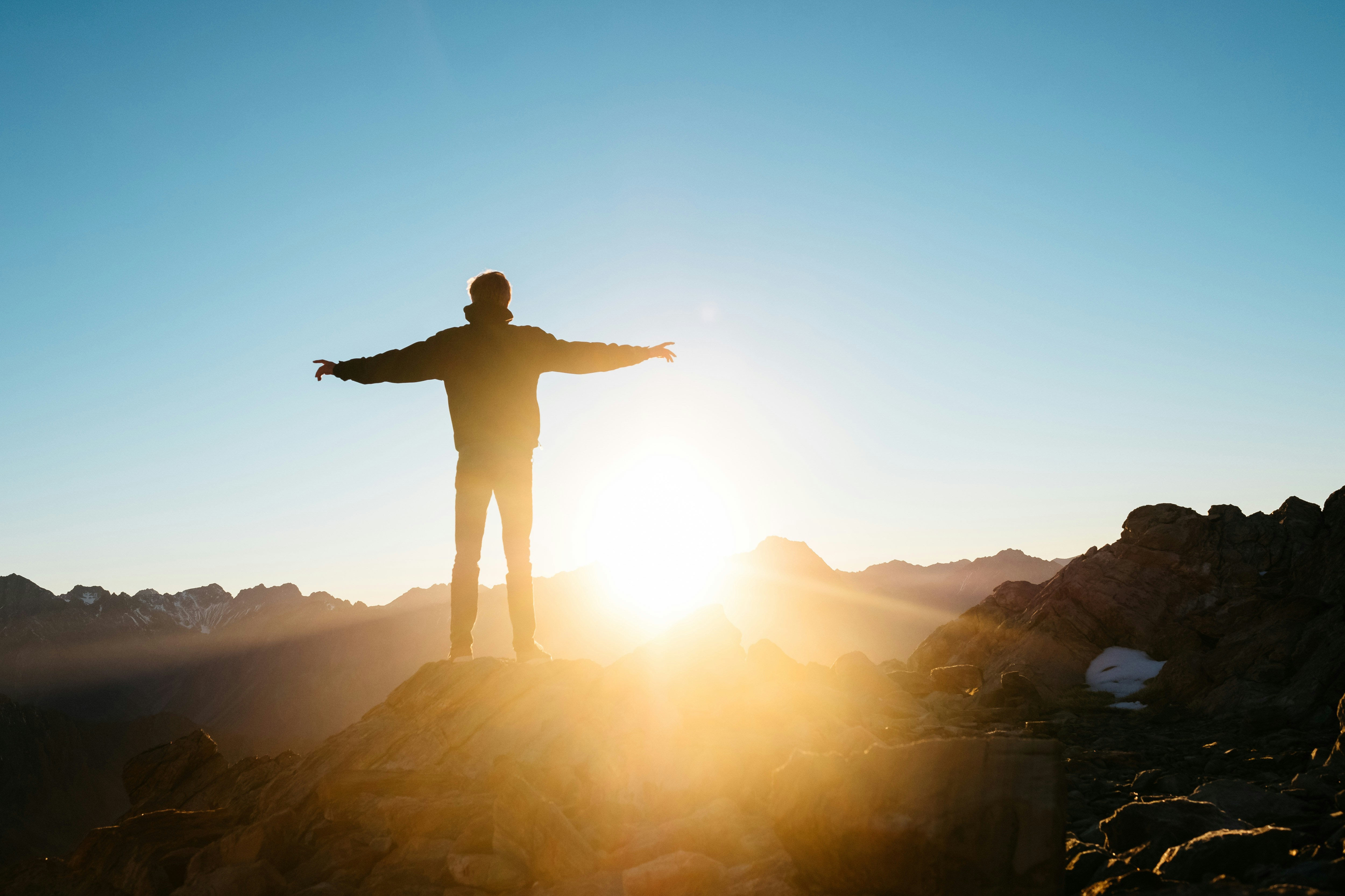 Person with arms outstretched on mountain at sunrise
